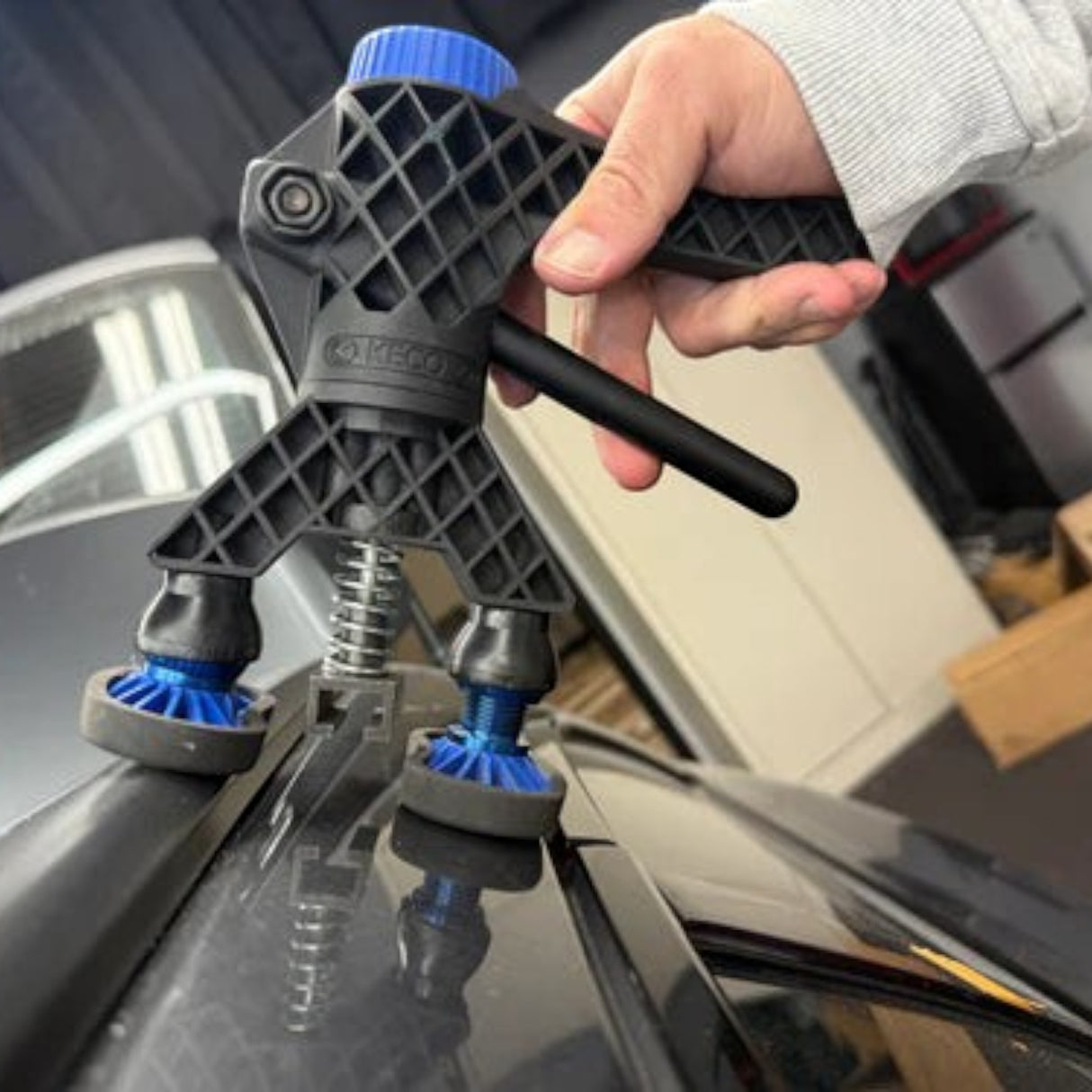 Anson PDR Black Plague Robo Legs with blue adjustable feet on a car panel for paintless dent repair.